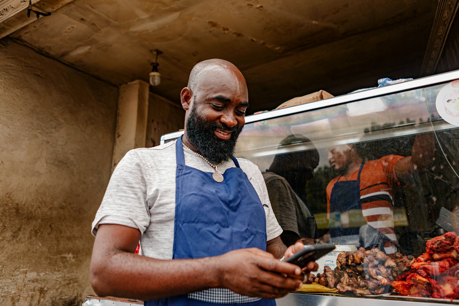 A food business owner in an apron checking an order on his phone